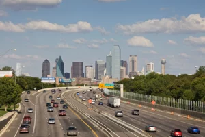 Wide-Angle View Of A Busy Dallas Freeway With Downtown Skyline In The Background, Illustrating The Urban Environment Where A Dallas Personal Injury Lawyer May Handle Traffic-Related Injury Claims.