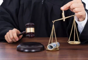 A Judge Holding A Gavel And A Symbolic Balance Scale With Rolled-Up Cash On One Side, Representing Financial Damages Awarded In A Legal Case.