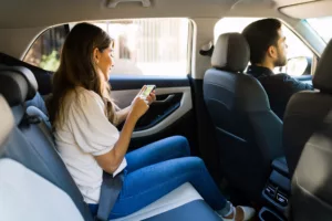 Smiling Passenger Sitting In The Backseat Of A Rideshare Vehicle With A Male Driver Up Front, Representing Situations Where An Arlington Uber Accident Lawyer Can Assist Injured Riders.